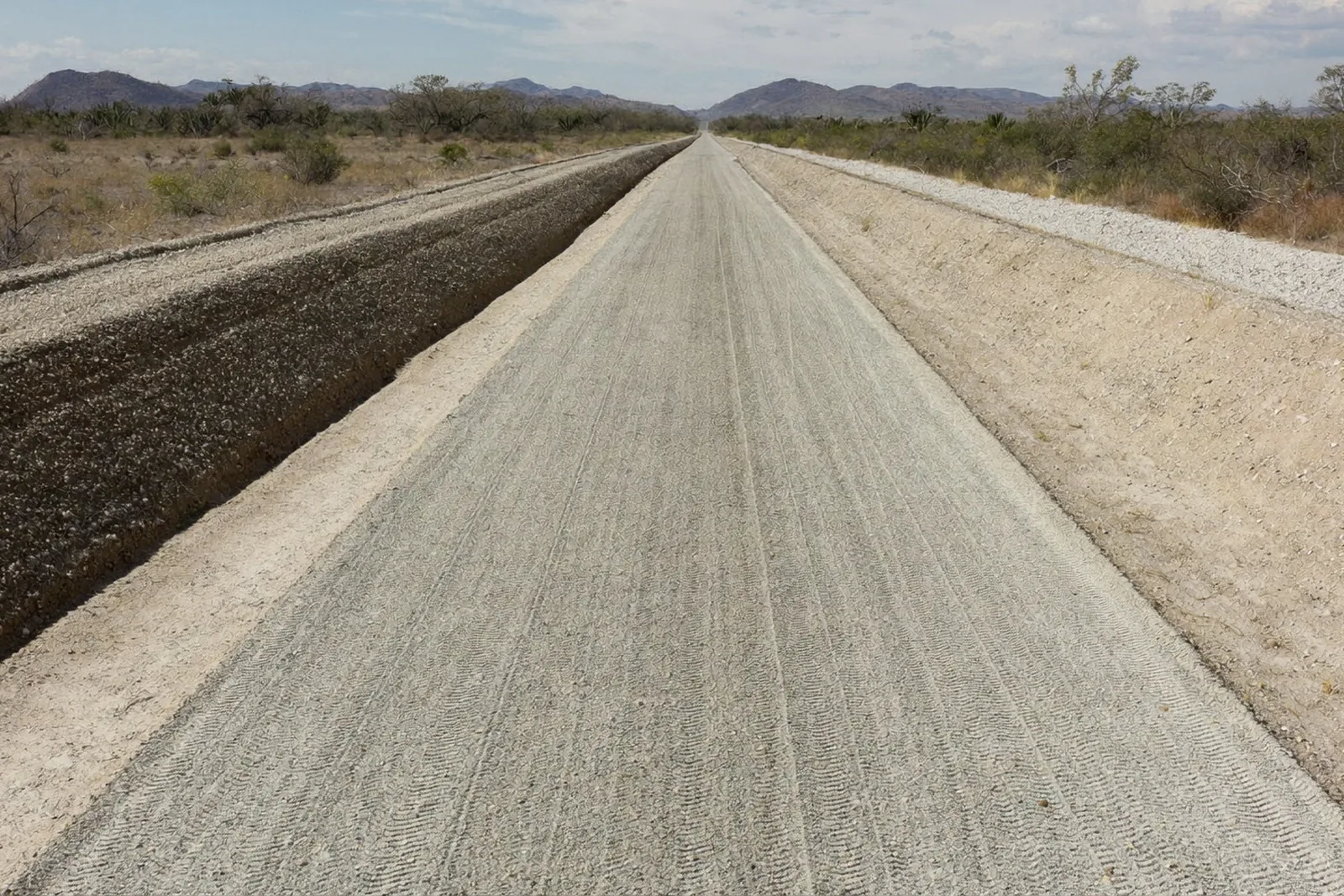 Freshly bladed gravel district road with a windrow along one edge and shaped side drains.