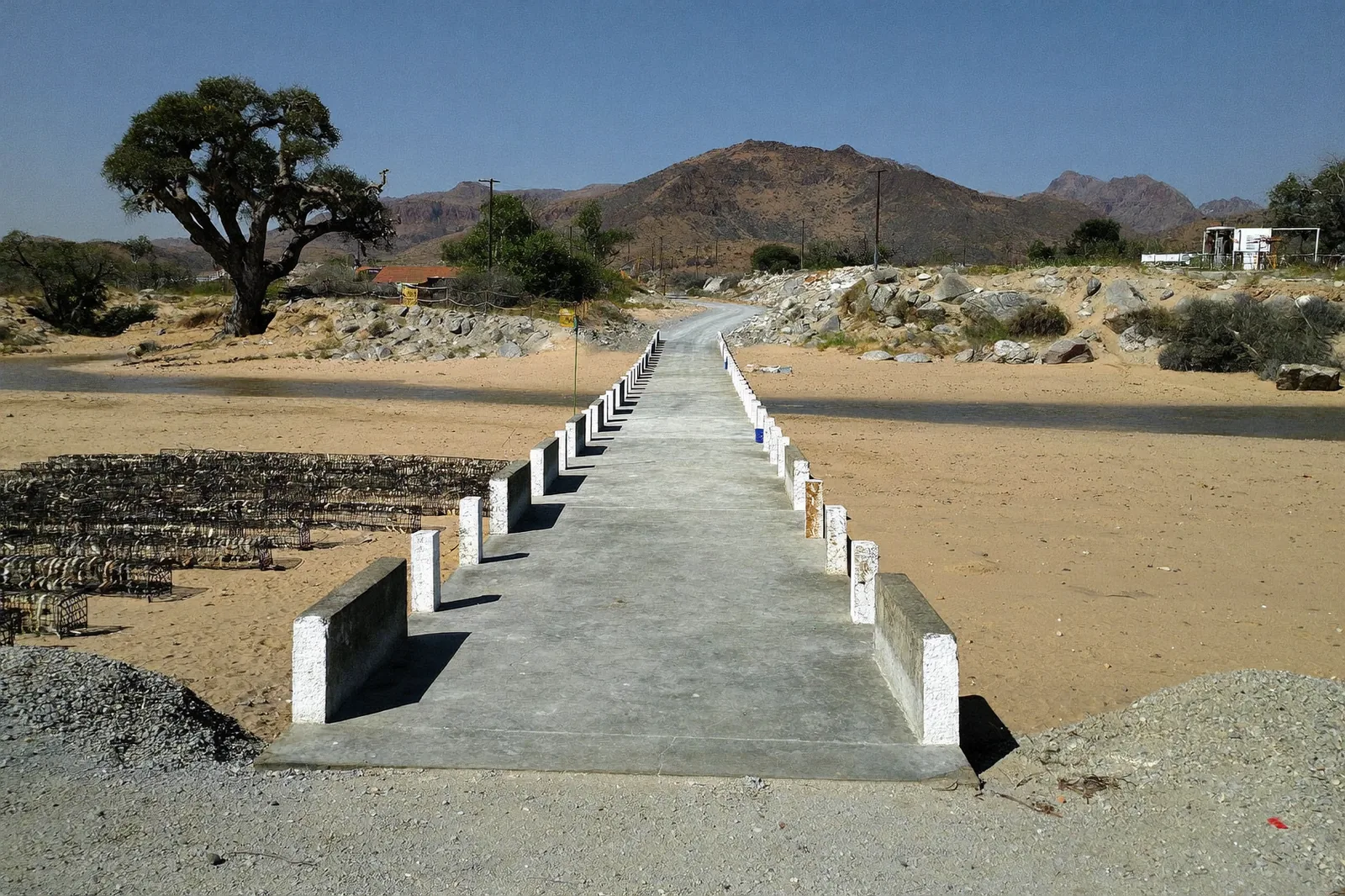 Concrete low-level causeway with white marker posts crossing a dry sandy riverbed in Kunene Region.