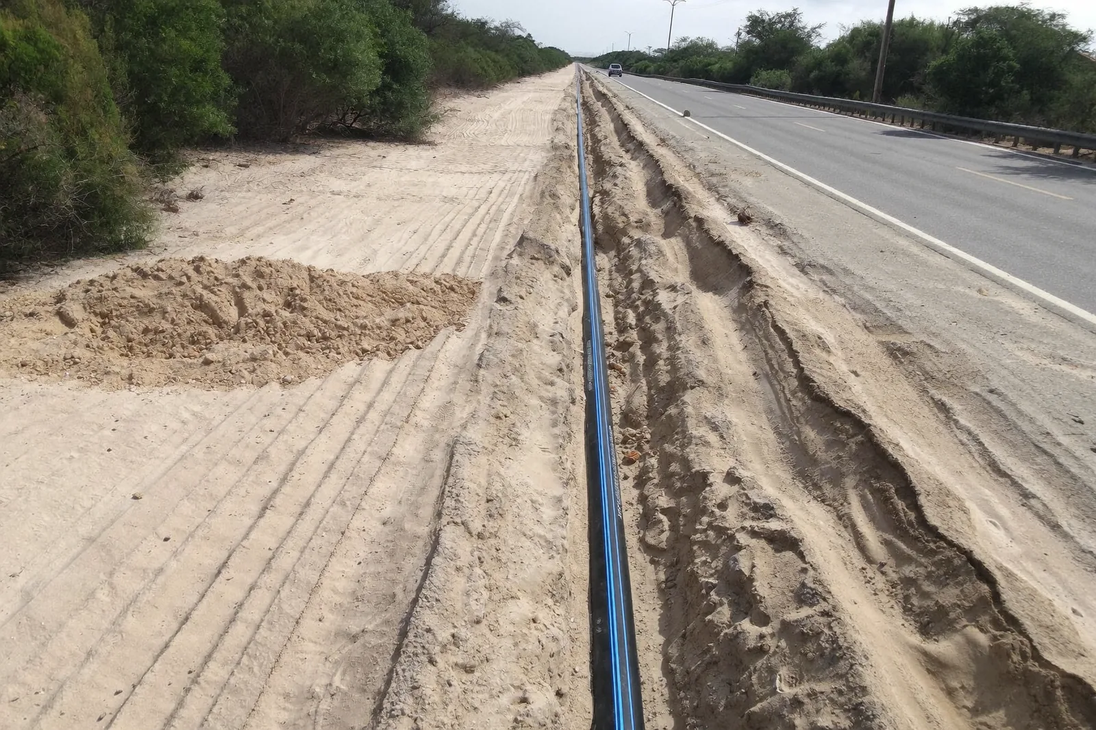HDPE water main laid in an open trench in Kalahari sand beside a tarred road.