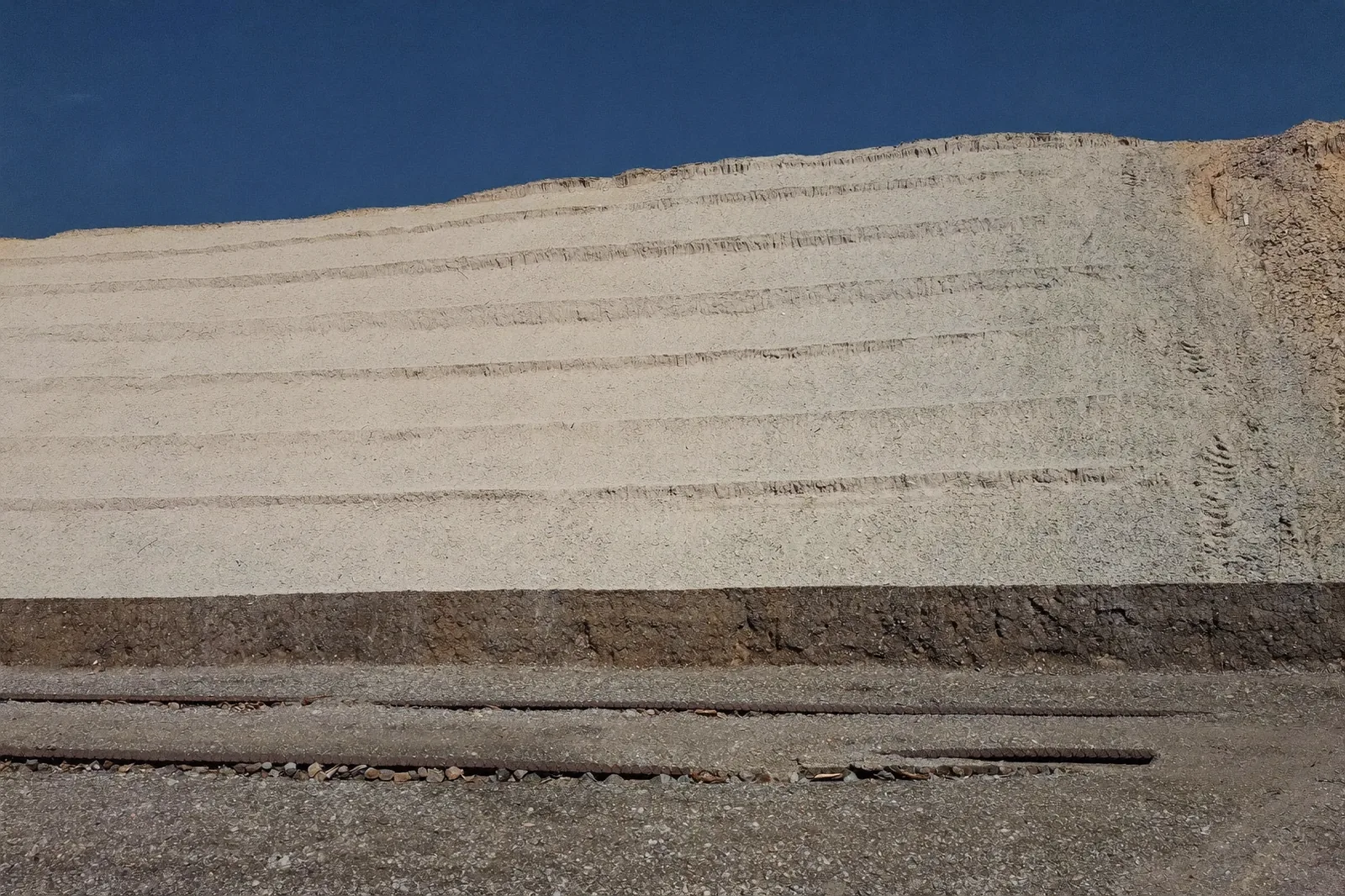Tailings dam wall rising in benched lifts with a rockfill buttress berm and toe track.