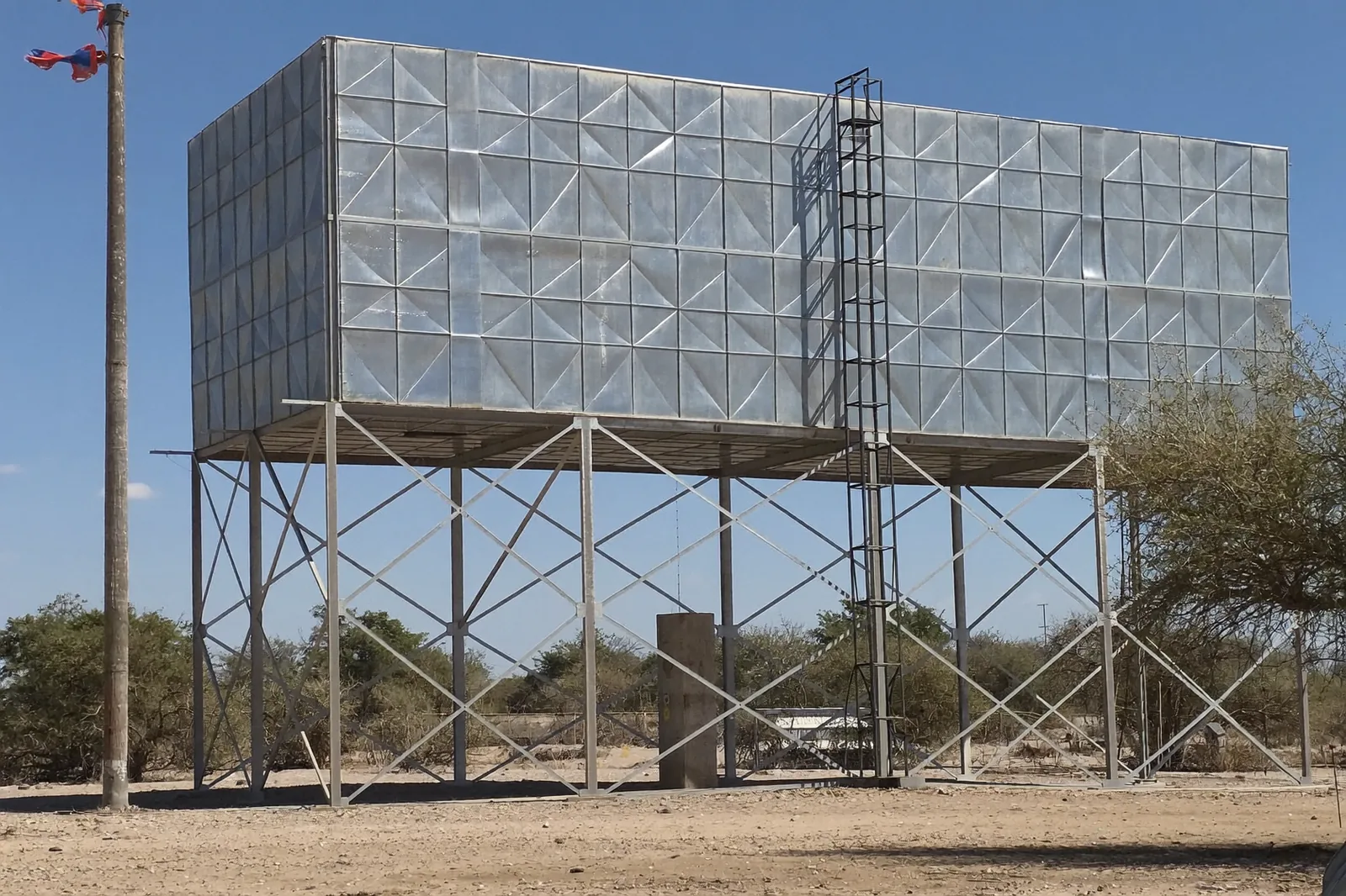 Rectangular pressed-steel panel water tank on a braced steel tower with a caged ladder.